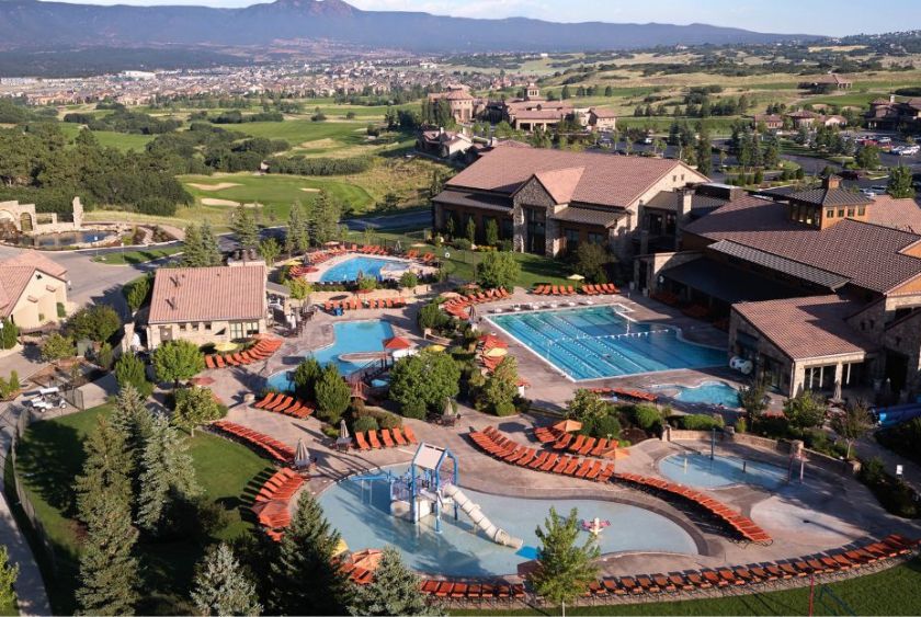Aerial view of a resort with multiple pools, lounge chairs, and buildings surrounded by greenery and distant mountains.